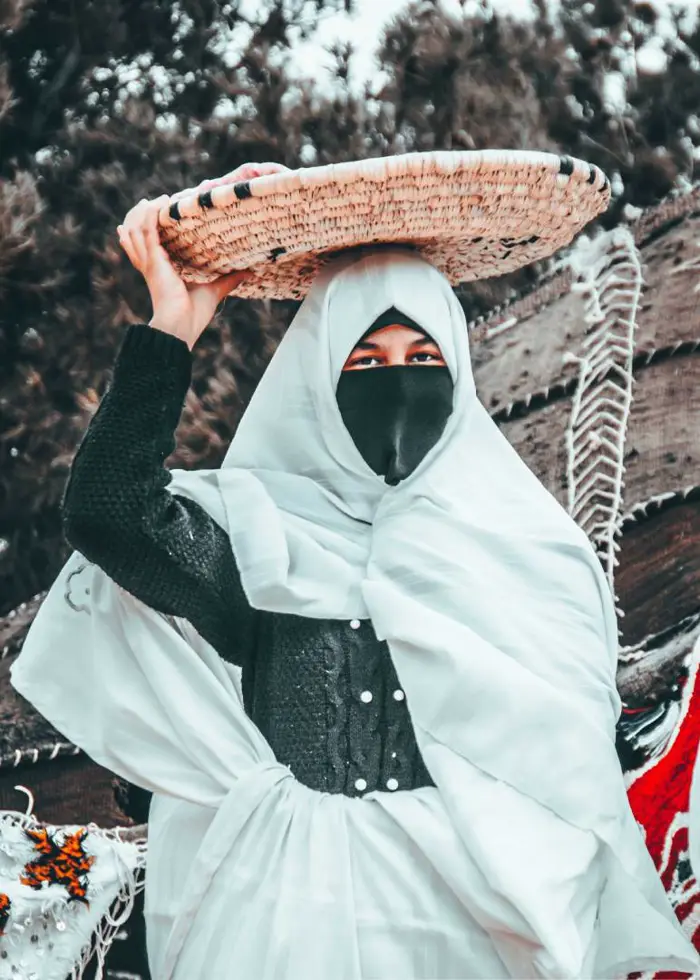 Une femme d’Itzer en haïk blanc porte un panier tressé sur la tête