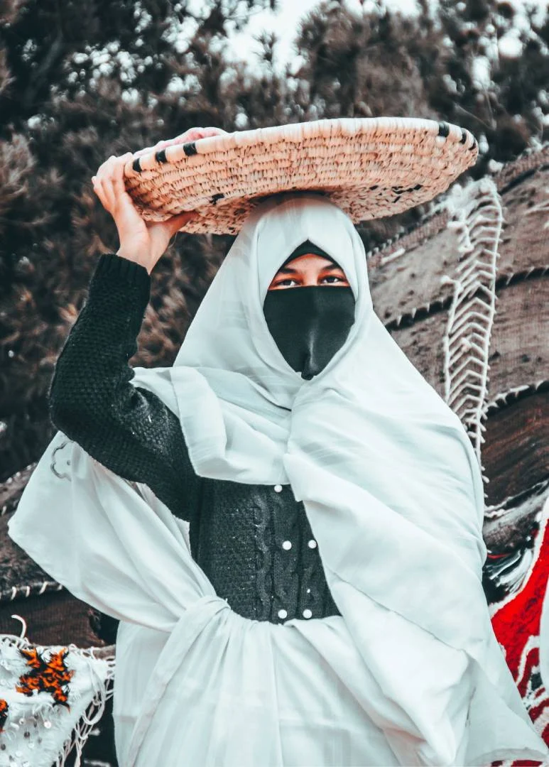 Une femme d’Itzer en haïk blanc porte un panier tressé sur la tête